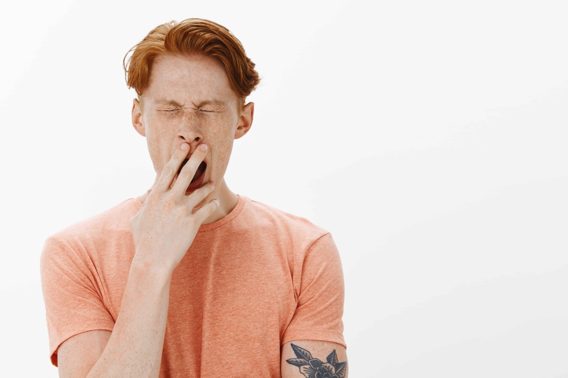 Here's a close-up image of a sleepy, redhead college man yawning, looking tired and as if he's just woken up early for classes.