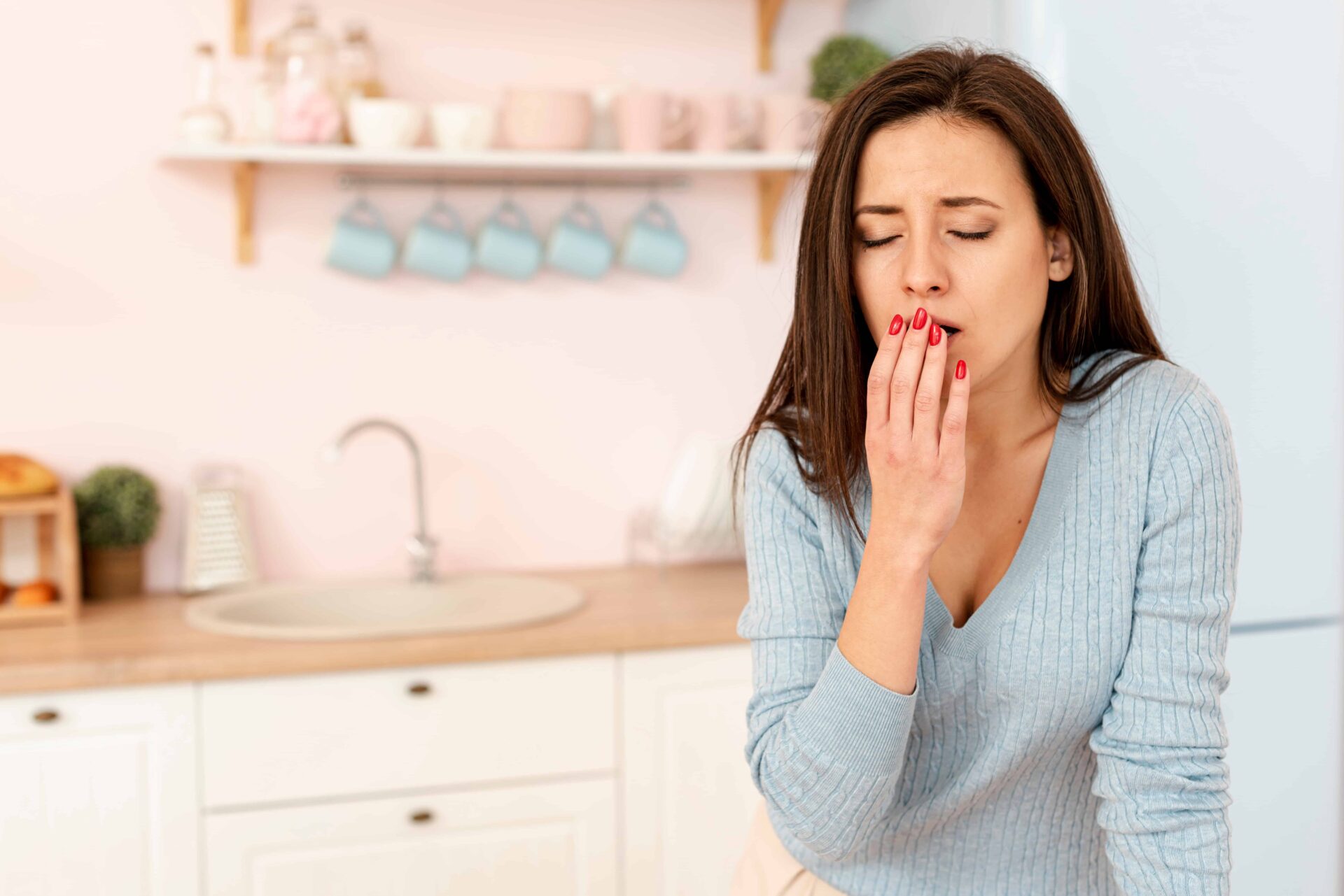 A medium-shot captures a woman in a kitchen, hunched over and coughing, with a look of discomfort on her face.